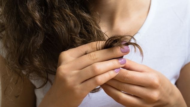 Mulher com cabelo cacheado utiliza óleo reparador de pontas em seus cabelos