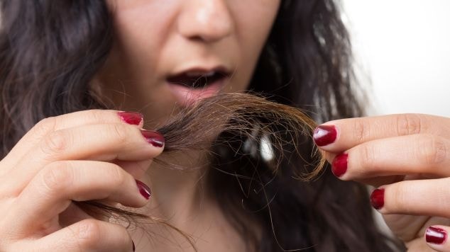 Mulher com cabelo danificado considera usar um reparador de pontas para proteger seus fios. 