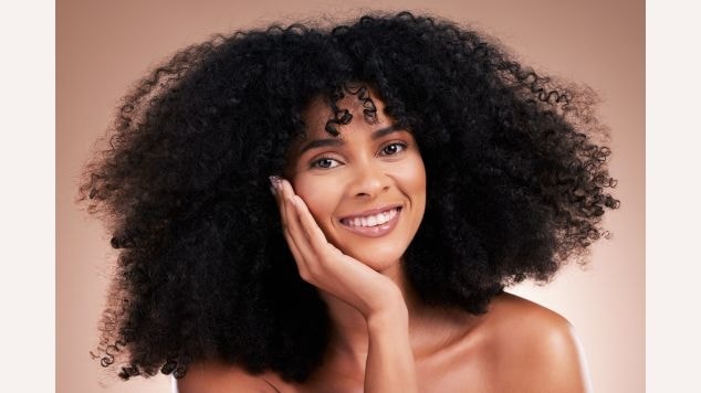 Mulher sorridente com a mão esquerda encostando em sua bochecha e cabelo cacheado volumoso.