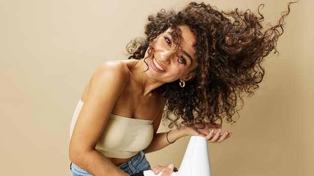 Mulher jovem de cabelos cacheados seca seu cabelo usando protetor térmico para cabelo