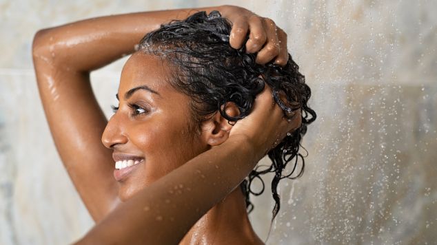 Mulher lavando o cabelo com shampoo anti residuo no banheiro.