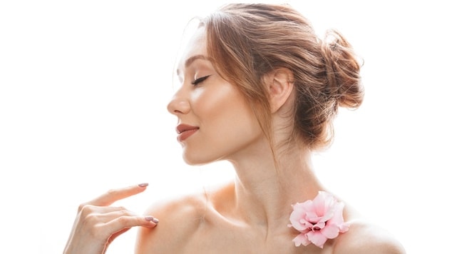 Mulher com coque despojado em cabelo curto com uma flor no ombro.