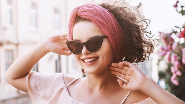 Mulher com lenço rosa na cabeça e óculos escuros.