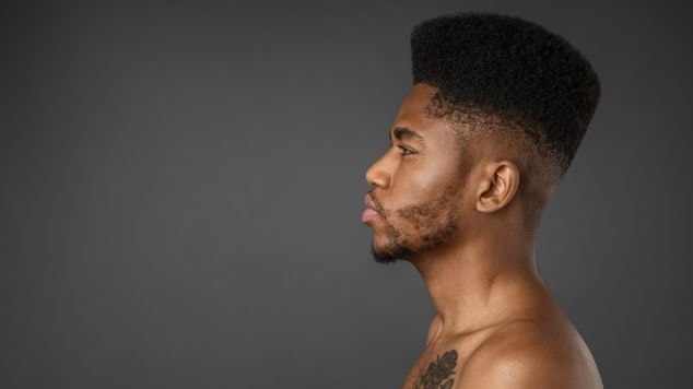 Homem virado para o lado esquerdo com tatuagem no peito.