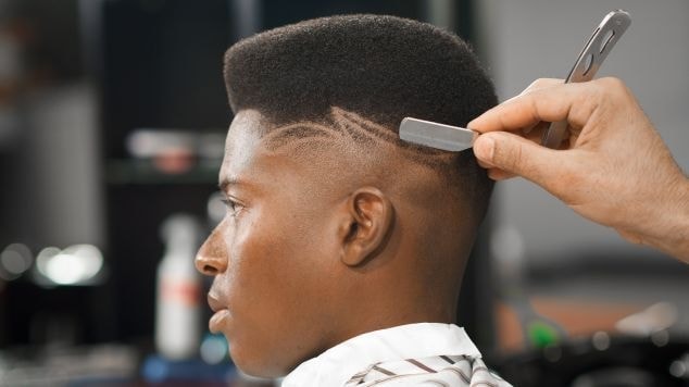 Homem fazendo corte com risco lateral em seu cabelo no salão.