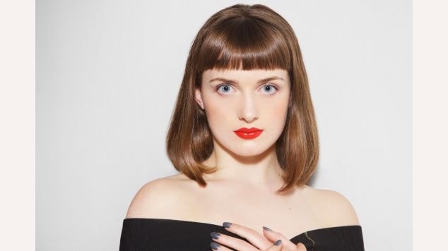 Mulher com corte bob clássico na altura do queixo em tom castanho médio com franja reta e curta acima das sobrancelhas, criando um visual retrô e elegante