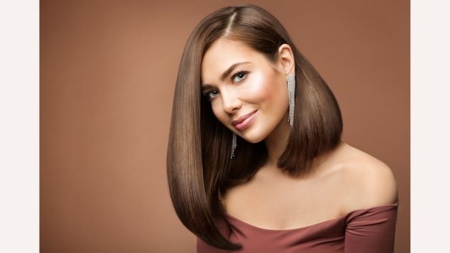 Mulher elegante com corte long bob assimétrico castanho médio extremamente liso e brilhante, com um lado mais longo que o outro criando uma linha diagonal dramática.