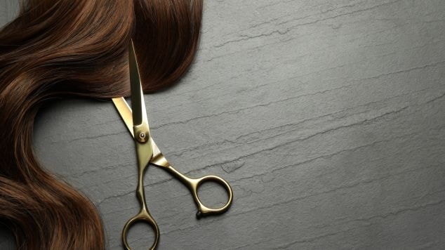 Tesoura cortando cabelo em fundo cinza. 