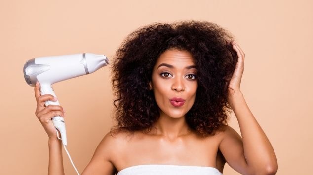 Mulher com cabelo cacheado usa secador e proteção térmica nos fios