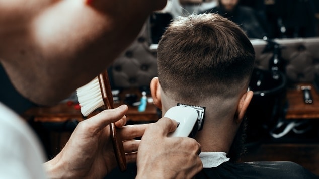 Barbeiro fazendo corte degradê em cabelo liso com máquina em cliente.