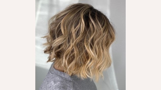 Mechas loiras no cabelo ondulado curto de uma jovem