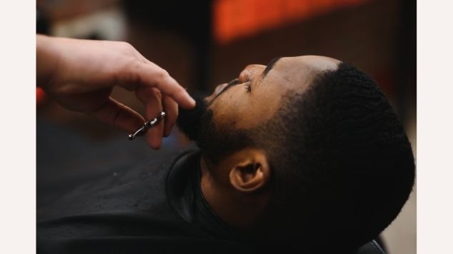 Homem aparando a barba com barbeiro para fazer baby hair harmônico em seu cabelo.