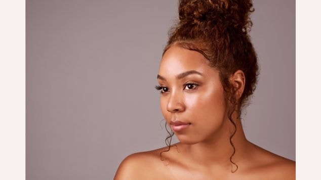 Mulher com cabelo cacheado ruivo em um coque com baby hair na testa.