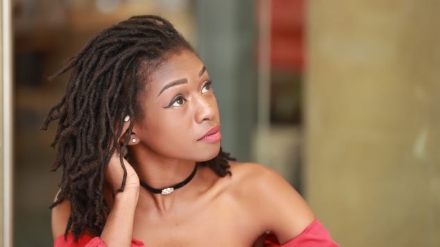 Mulher olhando para o lado direito com dreadlocks naturais em seu cabelo usando uma blusa de manga longa vermelha e gargantilha preta no pescoço.