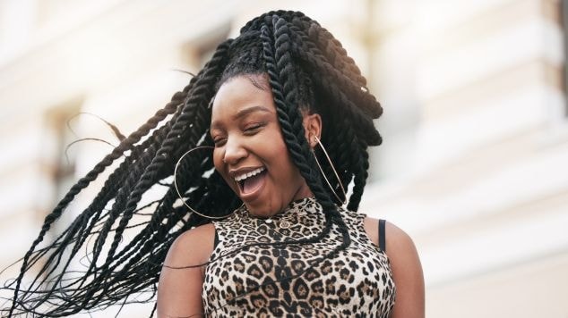 Mulher sorridente com top de oncinha e com tranças em seu cabelo.