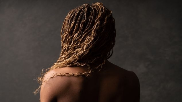 Foto de jovem mulher negra de costas com os cabelos com trança com cachos