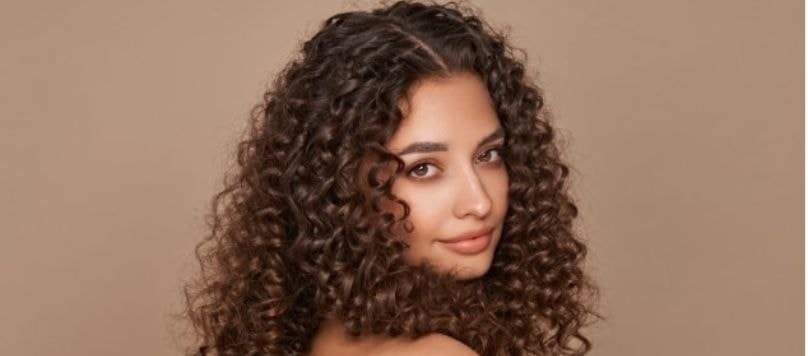 Jovem modelo com o cabelo cacheado chocolate avelã em fundo laranja.