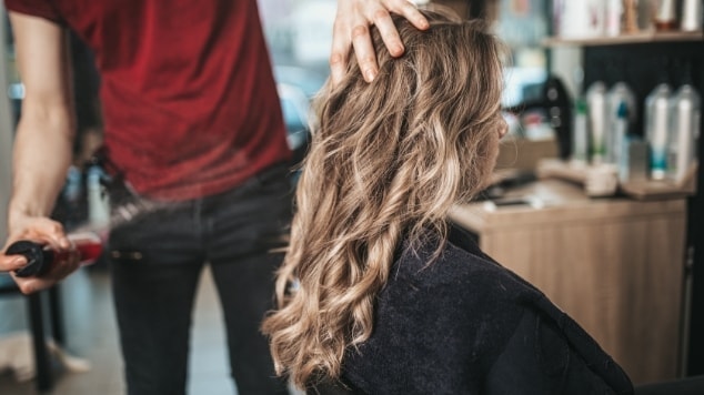 Profissional cabeleireiro finaliza a coloração de sua cliente no salão de beleza.