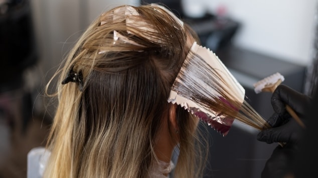 Profissional cabeleireiro realiza a descoloração no cabelo de sua cliente no salão de beleza.