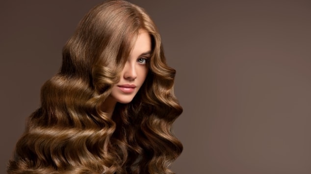 Mulher sorridente com o cabelo cor chocolate e vestido vermelho em fundo cinza