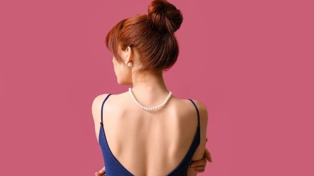 Jovem mulher de costas com o cabelo ruivo escuro em um coque alto.