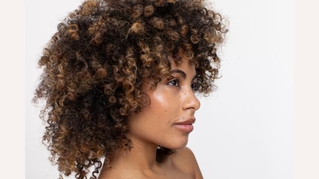 Mulher com o cabelo castanho e cacheado com pontas de tom loiro