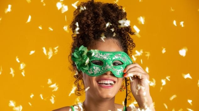 Mulher latina feliz e usando máscara carnavalesca com a cor do cabelo para o carnaval em tom castanho.