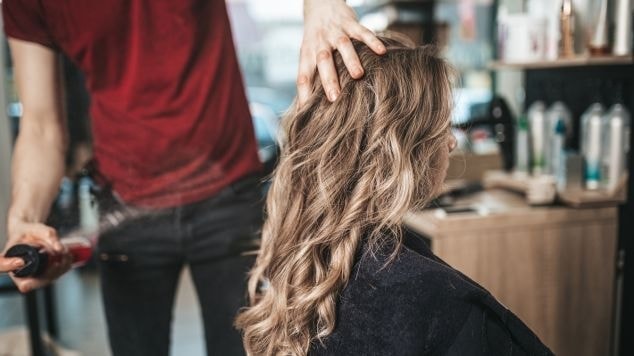 Profissional cabeleireiro finaliza a coloração com tinta sem amônia para cobrir cabelos brancos em sua cliente no salão de beleza.