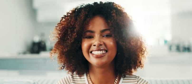 Mulher negra com cabelos cacheados sem frizz sorrindo para a câmera.