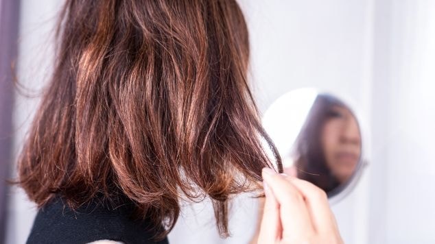 Mulher observa e analisa seu cabelo liso com frizz no espelho