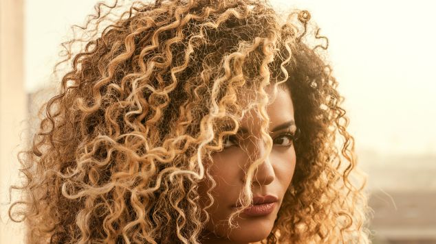 Jovem latina com o cabelo crespo utiliza defrizante em leave-in para acabar com o frizz no cabelo.