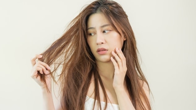 Jovem mulher analisa seus fios para identificar se há a presença de frizz no cabelo.