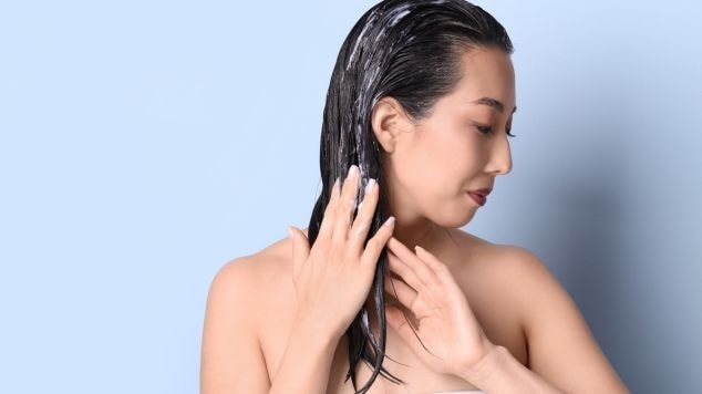 Mulher aplica máscara de hidratação no cabelo para repor umidade e mantê-lo macio.