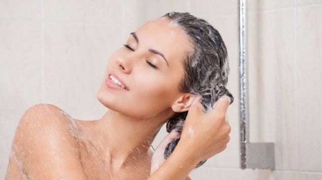 Mulher usa shampoo e condicionador hidratantes no cabelo durante o banho para realizar a limpeza capilar.