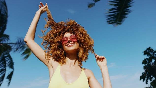 Jovem sorridente com o cabelo crespo mantém os fios protegidos para evitar o verde do cabelo.