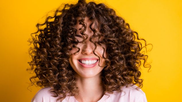 Mulher sorridente com o cabelo cacheado e reparado com o uso de queratina no cabelo.