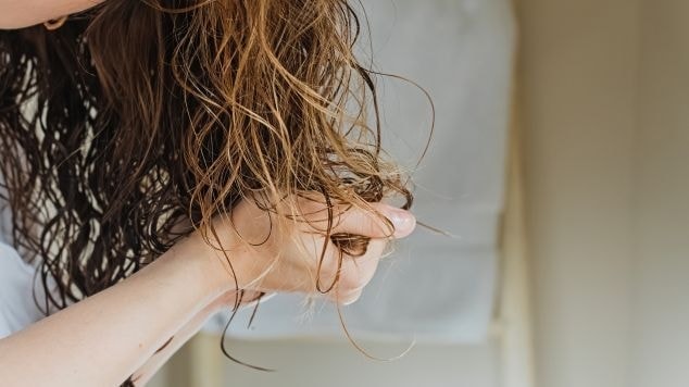 Mulher segurando os fios cacheados e molhados com a mão, em frente ao espelho, cuidando do cabelo após o banho como parte da rotina capilar.