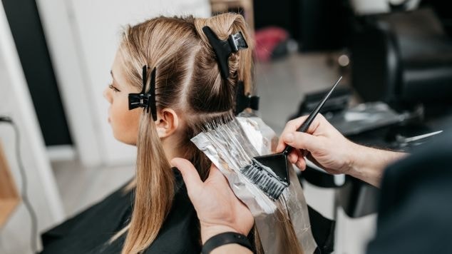 Profissional aplica tinta de cabelo em sua cliente com o cabelo loiro