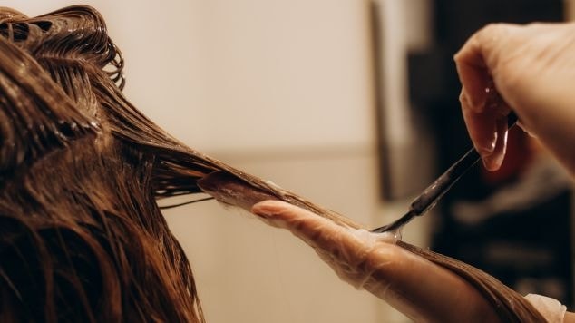 Profissional aplica tinta de cabelo em sua cliente com o cabelo pintado