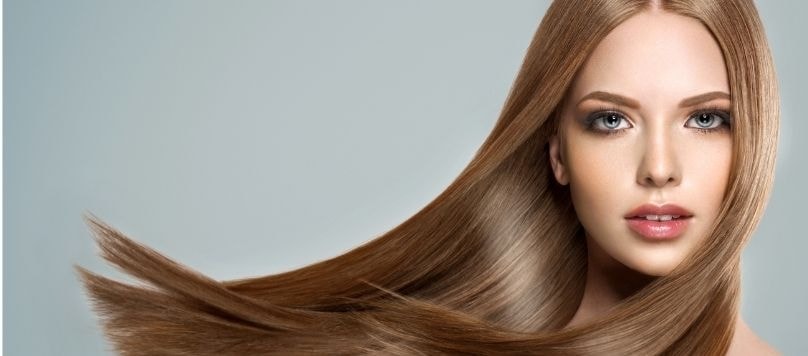 Mulher branca com cabelo loiro escuro liso e saudável após a selagem capilar.