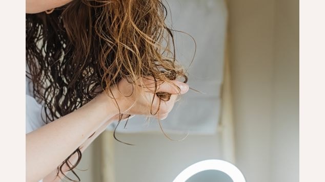 Mulher aplicando finalizador para a selagem do cabelo nos seus cachos.