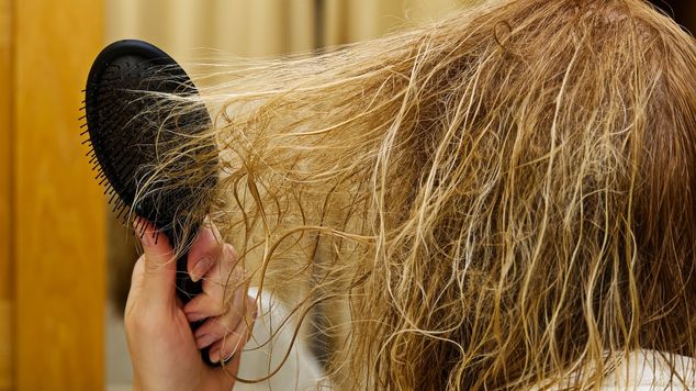 Mulher penteia seu cabelo elástico por conta da falta de proteínas na fibra capilar, como a queratina.