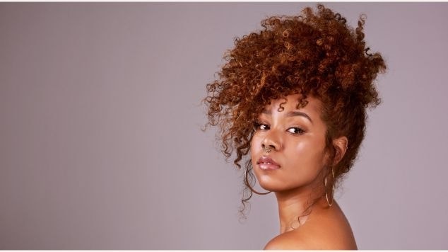 Mulher de perfil olhando para esquerda por cima do ombro de cabelo preso em um fundo cinza.