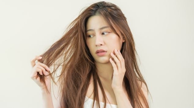 Mulher asiática com a mão no cabelo ressecado que pode tratar os fios com a recarga de queratina.