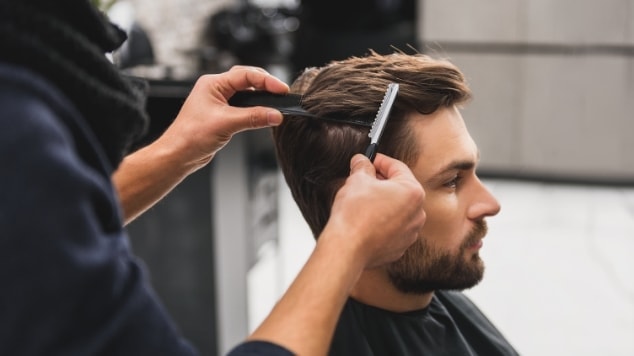 Profissional barbeiro realiza um corte de cabelo liso masculino em seu cliente na barbearia.