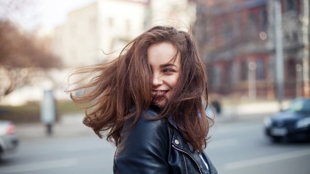 Jovem mulher branca e sorridente com cabelo liso de cor castanho balançando ao vento.