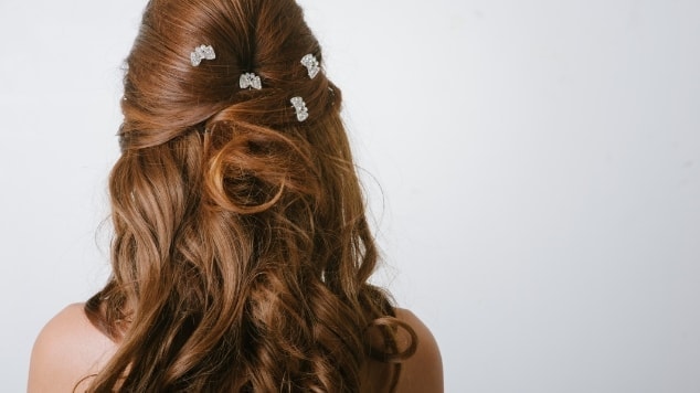 Mulher de costas destacando seu cabelo ondulado em fundo neutro.