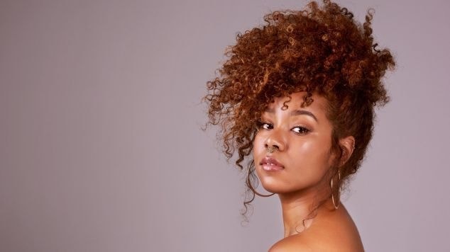 Mulher séria com um penteado em seu cabelo cacheado, uma das possibilidades de curvaturas de cabelo.