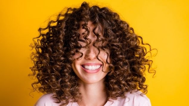 Jovem sorridente com um corte de cabelo cacheado moderno e atual em fundo amarelo.