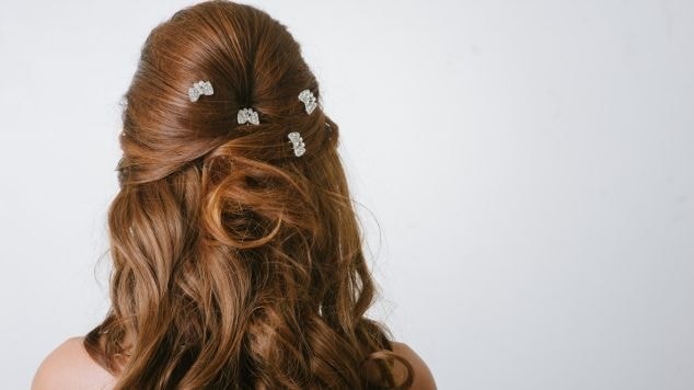 Mulher de costas com o cabelo cor de avelã meio preso por um penteado em um fundo branco.
